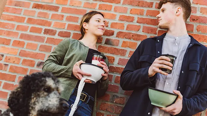 ORNAMIN-Zwei junge Menschen unterwegs in der Stadt mit ORNAMIN To go Mehrwegschale und Coffee To go Mehrwegbecher